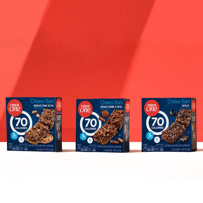 Three boxes of Fiber One Chewy Bars on a white surface with a red background