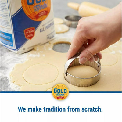 Person cutting out shapes from dough with a cookie cutter, Gold Medal flour in the background.