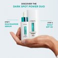 Hand holding two bottles of a skincare product with a blurred background