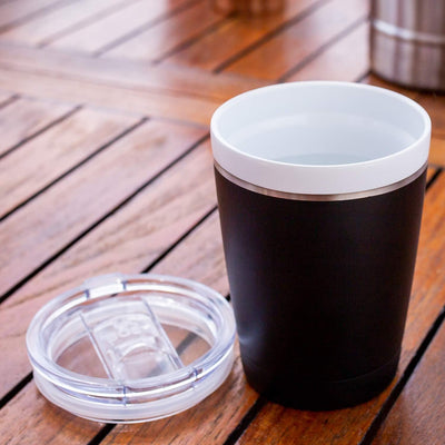 Black insulated tumbler with a white lid on a wooden surface